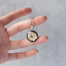 Hand holding a round steampunk necklace made with watch parts