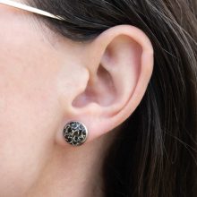 Close-up of a steampunk stud earring worn on an ear, showing real watch parts in resin.