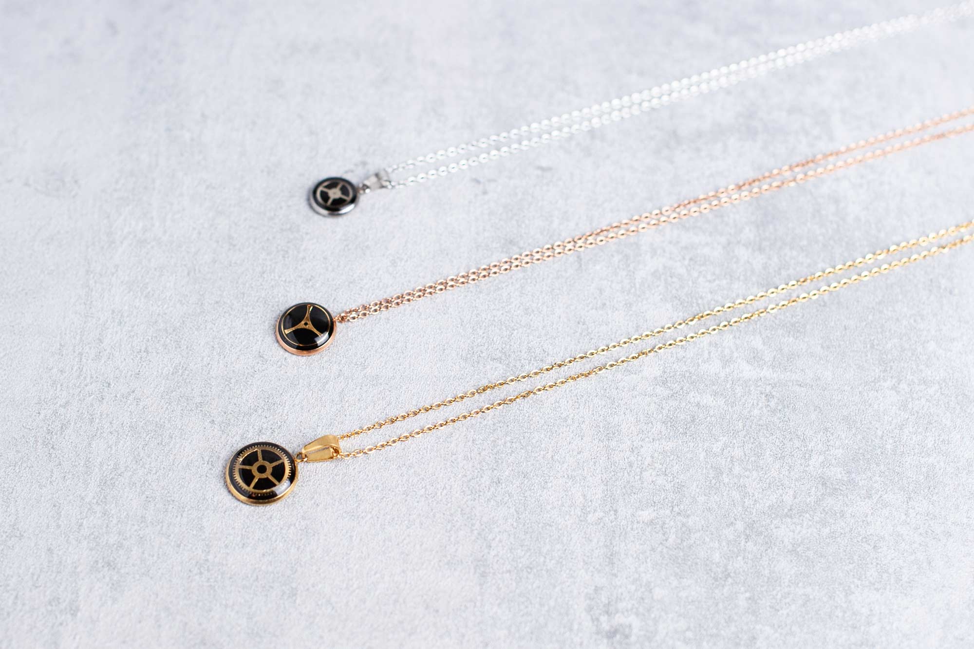 Three minimalist steampunk necklaces with watch gears in rose gold, gold, and silver